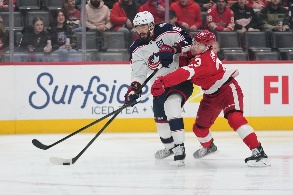Columbus Blue Jackets right wing Kirill Marchenko (86) shoots as Detroit Red Wings left wing Lucas Raymond (23) defends in the first period of an NHL hockey game Tuesday, April 7, 2026, in Detroit. (AP Photo/Paul Sancya)