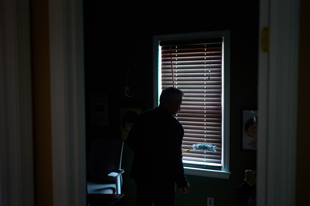 Chris Colocousis, who is still so shaken by a scam that took his retirement savings that he sometimes has trouble leaving his house, cleans the blinds in his home, Wednesday, March 11, 2026, in Raynham, Mass. (AP Photo/David Goldman)
