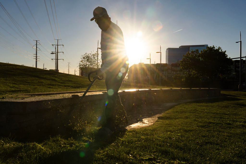 A City of Tempe Parks and Recreation Department groundskeeper manicures grass as the sun rises at Tempe Town Lake on Thursday, March 19, 2026, in Tempe, Ariz. (AP Photo/Rebecca Noble)