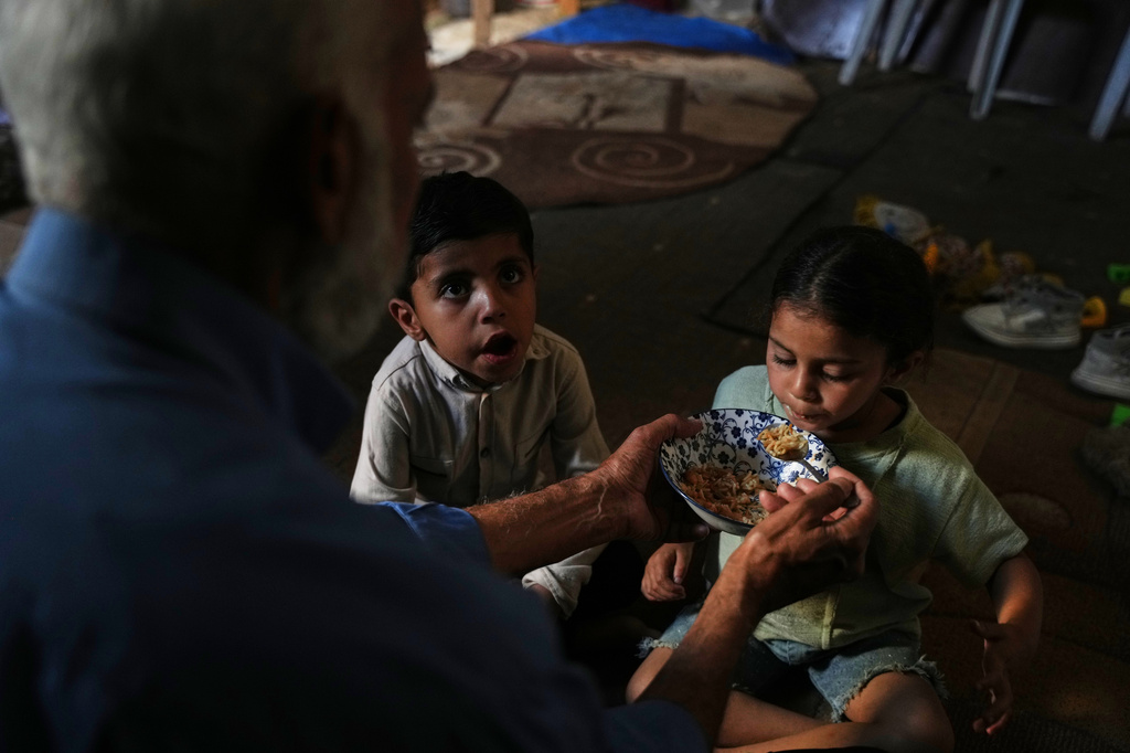 Mahmoud Nofal, 64, feeds his grandchildren, Tamim and Raneen Nofal, whom he has raised since their parents were killed in an Israeli airstrike, in Khan Younis, southern Gaza Strip, June 2, 2026. (AP Photo/Abdel Kareem Hana)
