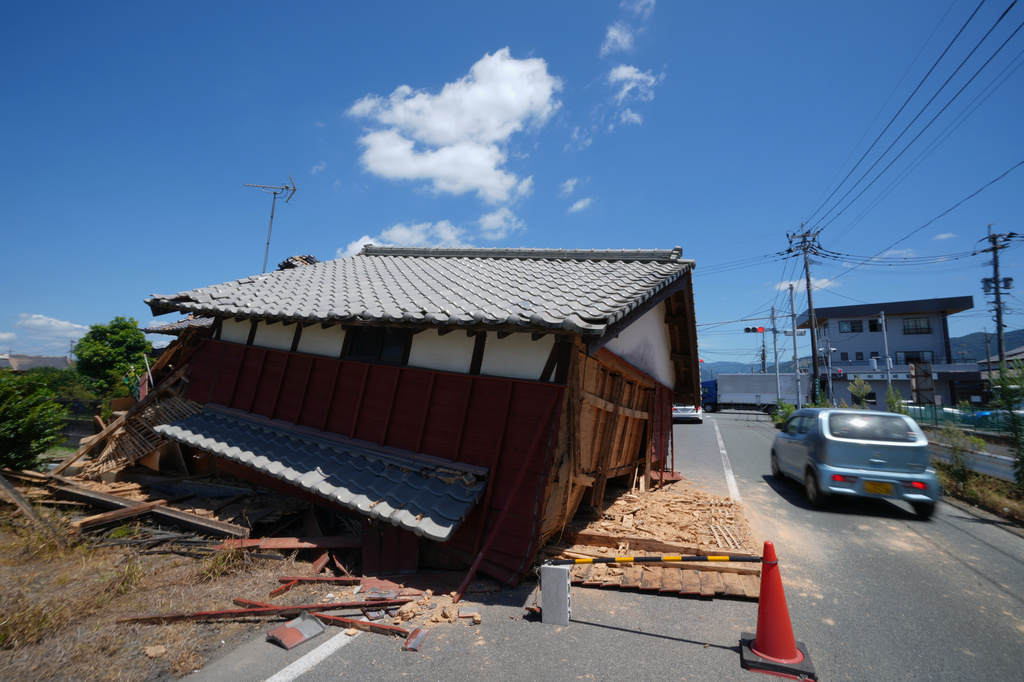 A car moves to the wrong lane to avoid a damaged building that fell on the street in Yatsushiro, southern Japan, Friday, July 31, 2026, three days after an earthquake hit the area. (AP Photo/Hiro Komae)
