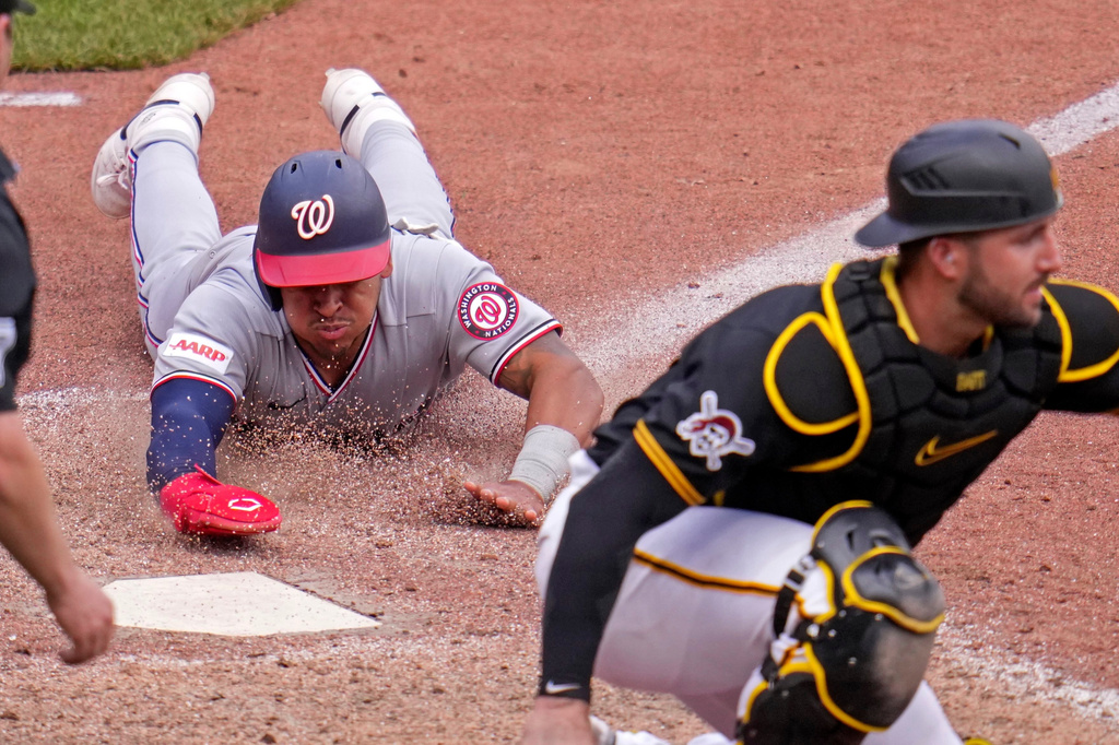 Washington Nationals' Jorbit Vivas, left, slides into home as Pittsburgh Pirates catcher Joey Bart, right, waits for a late relay throw on a single by Nationals' James Wood off Pirates pitcher Dennis Santana during the 10th inning of a baseball game in Pittsburgh, Thursday, April 16, 2026. (AP Photo/Gene J. Puskar)