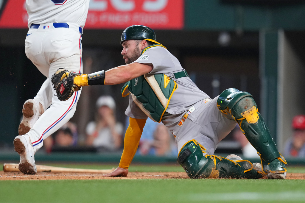 Athletics catcher Austin Wynns, right, is late on the tag as Texas Rangers' Danny Jansen scores on an RBI fly ball hit by Brandon Nimmo during the third inning of a baseball game Saturday, April 25, 2026, in Arlington, Texas. (AP Photo/Julio Cortez)
