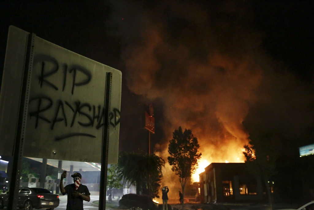 FILE- In this June 13, 2020 file photo, "RIP Rayshard" is spray-painted on a sign as flames engulf a Wendy's restaurant where Rayshard Brooks was shot and killed by police in Atlanta. (AP Photo/Brynn Anderson, File)