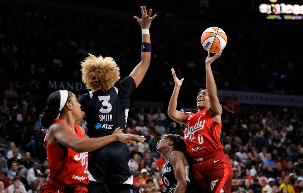 Indiana Fever guard Kelsey Mitchell (0) shoots over Las Vegas Aces guard Jackie Young (0) as forward NaLyssa Smith (3) defends during the first half of an WNBA basketball game Sunday, July 12, 2026, in Las Vegas. Indiana Fever forward Monique Billings is at left. (Steve Marcus/Las Vegas Sun via AP)