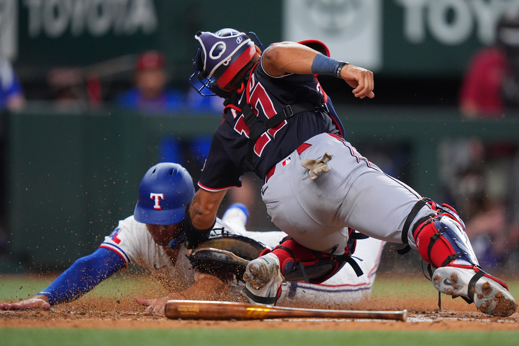 Texas Rangers' Wyatt Langford, left, scores on a fielders choice against Washington Nationals catcher Harry Ford during the third inning of a baseball game, Tuesday, Aug. 18, 2026, in Arlington, Texas. (AP Photo/LM Otero)