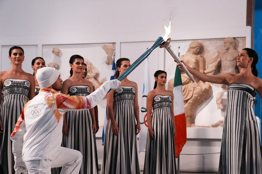 Actress Mary Mina, right, playing the role of high priestess, passes the Olympic flame to the first torchbearer Greek rower Petros Gaidatzis, during the flame lighting ceremony for the Milan Cortina 2026 Winter Olympics, at the archaeological museum of Olympia, Greece, Wednesday, Nov. 26, 2025. (AP Photo/Thanassis Stavrakis)