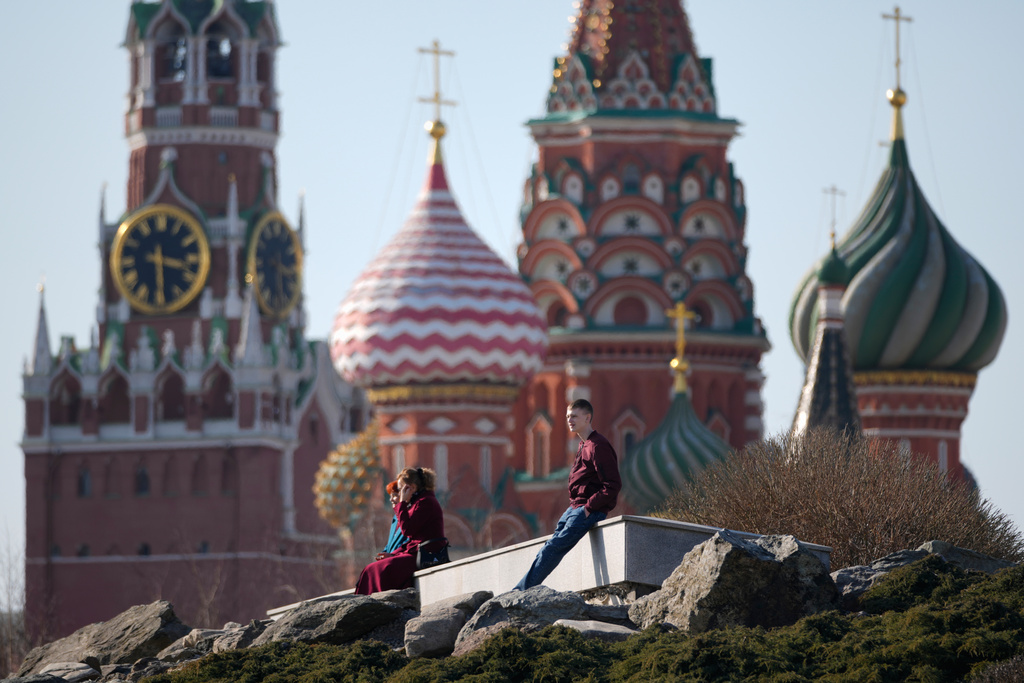 People enjoy warm weather as they sit at Zaryadye park in Moscow, Tuesday, March 24, 2026, backdropped by the Spasskaya tower of the Kremlin and St. Basil's Cathedral. (AP Photo/Pavel Bednyakov)