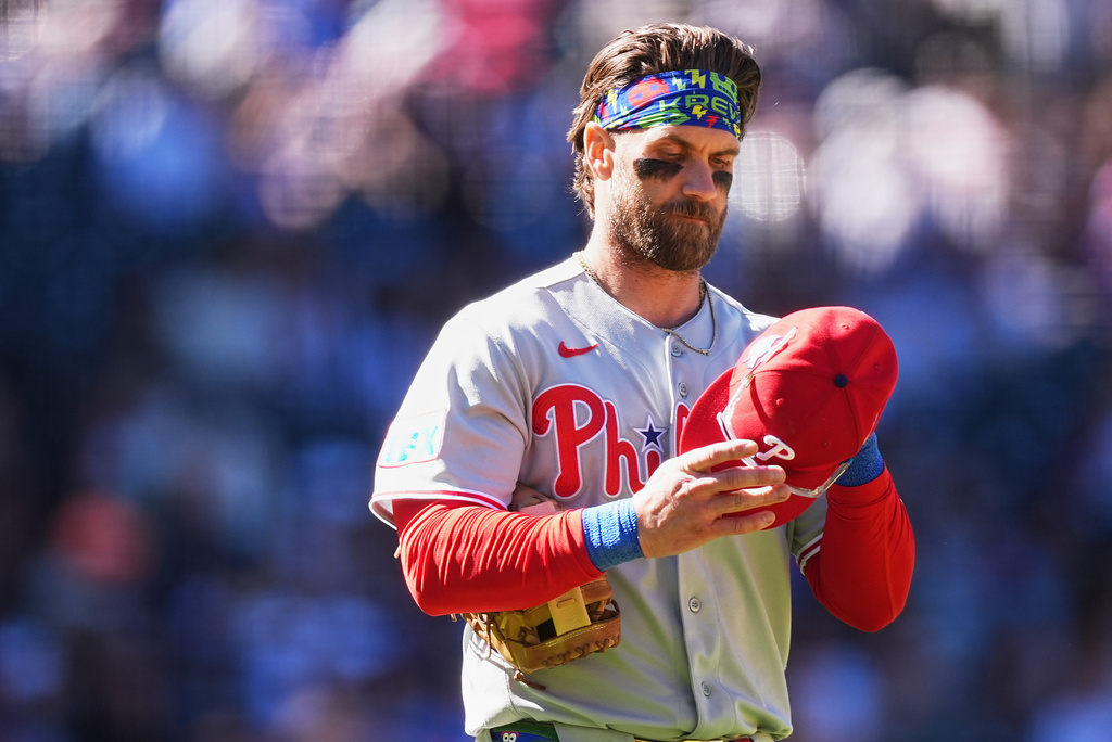Philadelphia Phillies first baseman Bryce Harper puts on his hat and heads to his position after lining out to end the top of the eighth inning of a baseball game against the Colorado Rockies Sunday, April 5, 2026, in Denver. (AP Photo/David Zalubowski)