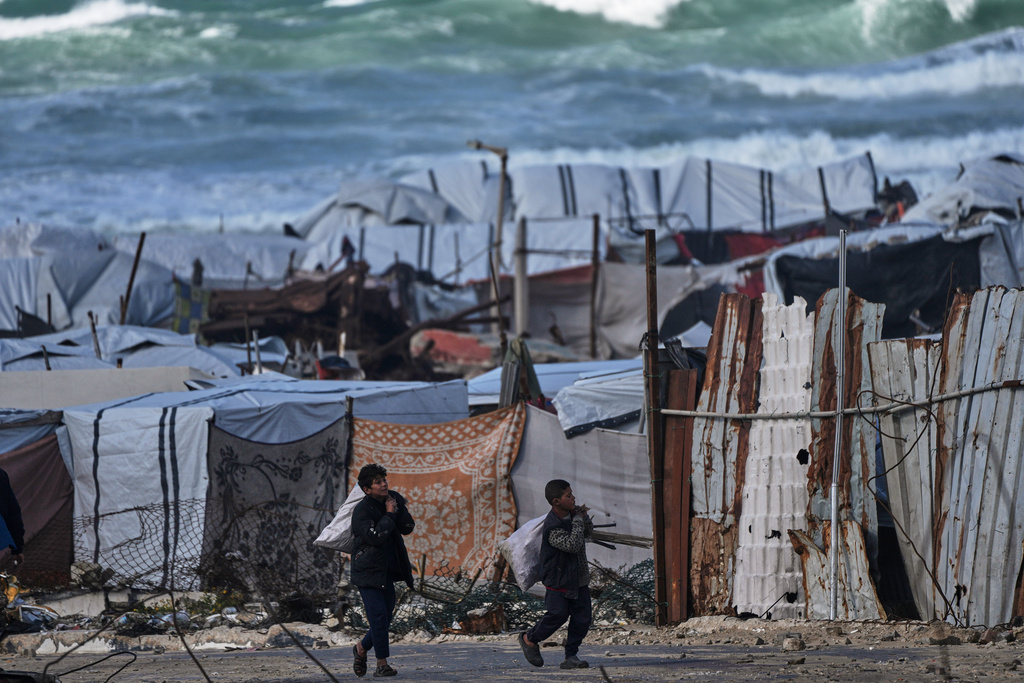 Palestinian children carry sacks filled with firewood as they walk through a displacement camp in Gaza City, Sunday, Dec. 28, 2025. (AP Photo/Jehad Alshrafi)