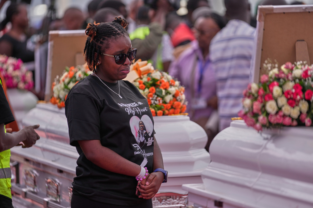 A relative grieves while standing between caskets carrying the remains of girls who died in the Utumishi Academy school fire during a memorial service at Gilgil Stadium, Nakuru County, Kenya, Friday, June 12, 2026. (AP Photo/Brian Inganga)