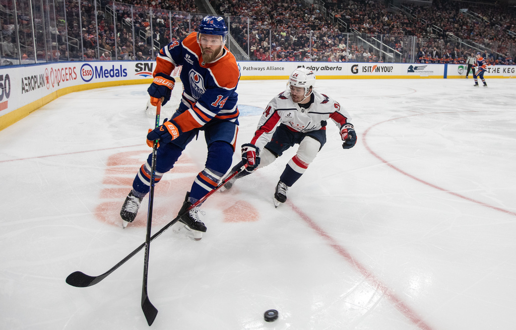 Washington Capitals' Connor McMichael (24) and Edmonton Oilers' Mattias Ekholm (14) battle for the puck during the first period of an NHL game, in Edmonton on Saturday, Jan. 24, 2026. (Jason Franson/The Canadian Press via AP)