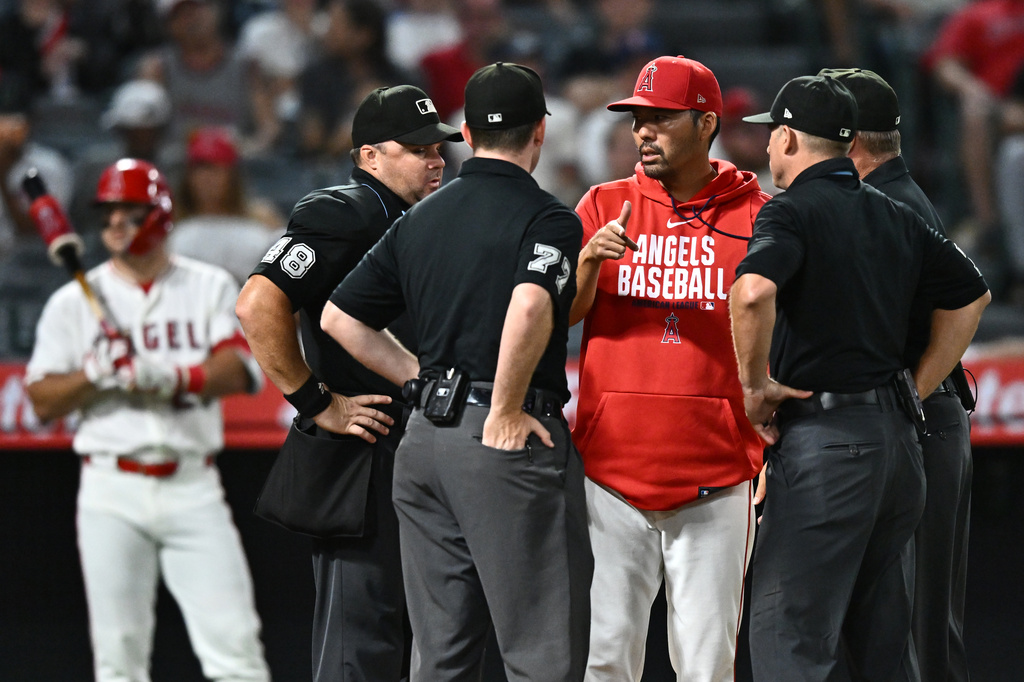 Los Angeles Angels manager Kurt Suzuki, center, speaks with the umpires during the seventh inning of a baseball game against the Texas Rangers, Monday, Aug. 10, 2026, in Anaheim, Calif. (AP Photo/William Liang)