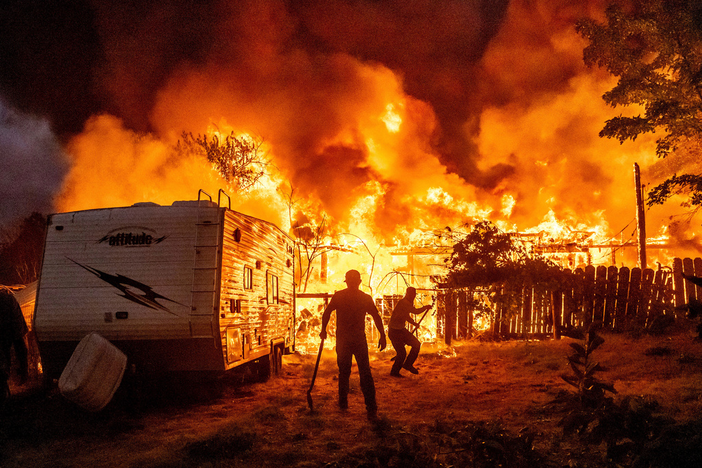 Residents work to stop flames from a burning home from spreading to a neighboring house as the 6-5 Fire burns through the Chinese Camp community of Tuolumne County, Calif., Sept. 2, 2025. (AP Photo/Noah Berger, File)