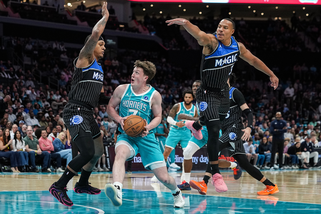 Charlotte Hornets guard Kon Knueppel (7) attempts to drive to the basket between Orlando Magic forward Paolo Banchero, left, and guard Desmond Bane (3) during the first half of an NBA basketball game, Thursday, March 19, 2026, in Charlotte, N.C. (AP Photo/Matt Kelley)