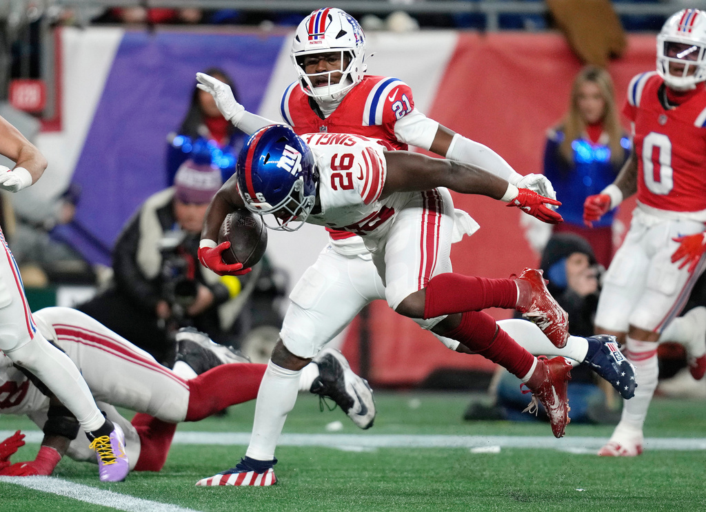 New York Giants running back Devin Singletary (26) scores a touchdown against New England Patriots safety Jaylinn Hawkins (21) during the second half of an NFL football game Monday, Dec. 1, 2025, in Foxborough, Mass. (AP Photo/Charles Krupa)
