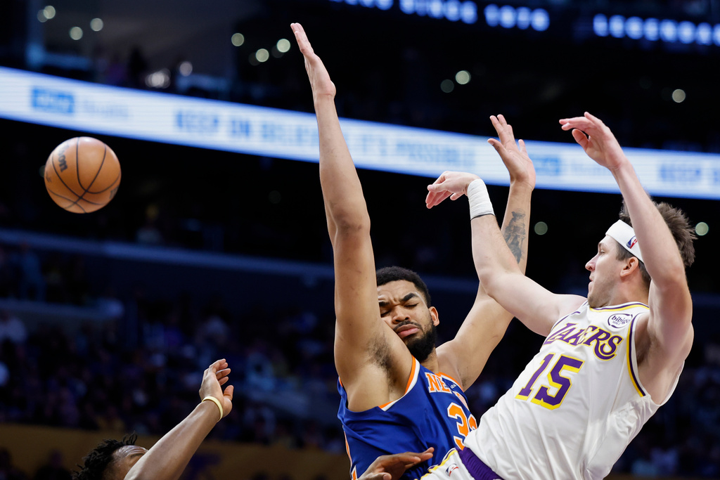 Los Angeles Lakers guard Austin Reaves (15) passes the ball to a teammate while being guarded by by New York Knicks center Karl-Anthony Towns during the first half of an NBA basketball game, Sunday, March 8, 2026, in Los Angeles. (AP Photo/Caroline Brehman)
