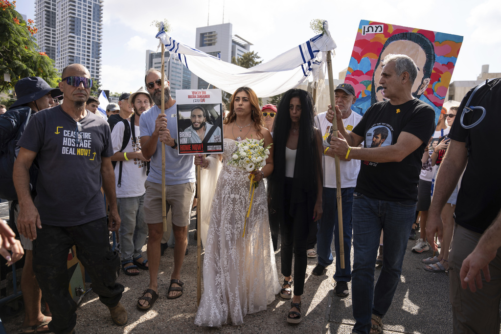 Holding a sign with a photo of her partner, Matan Zangauker, who is held hostage by Hamas, Ilana Gritzewsky, center left, is accompanied by his mother, Einav Zangauker, center right, as they arrive for a symbolic wedding ceremony at the plaza known as the hostages square in Tel Aviv, Israel, Sunday, Aug. 17, 2025, during a protest demanding the immediate release of all hostages and calling for the Israeli government to reverse its decision to take over Gaza City and other areas in the Gaza Strip.(AP Photo/Maya Levin)