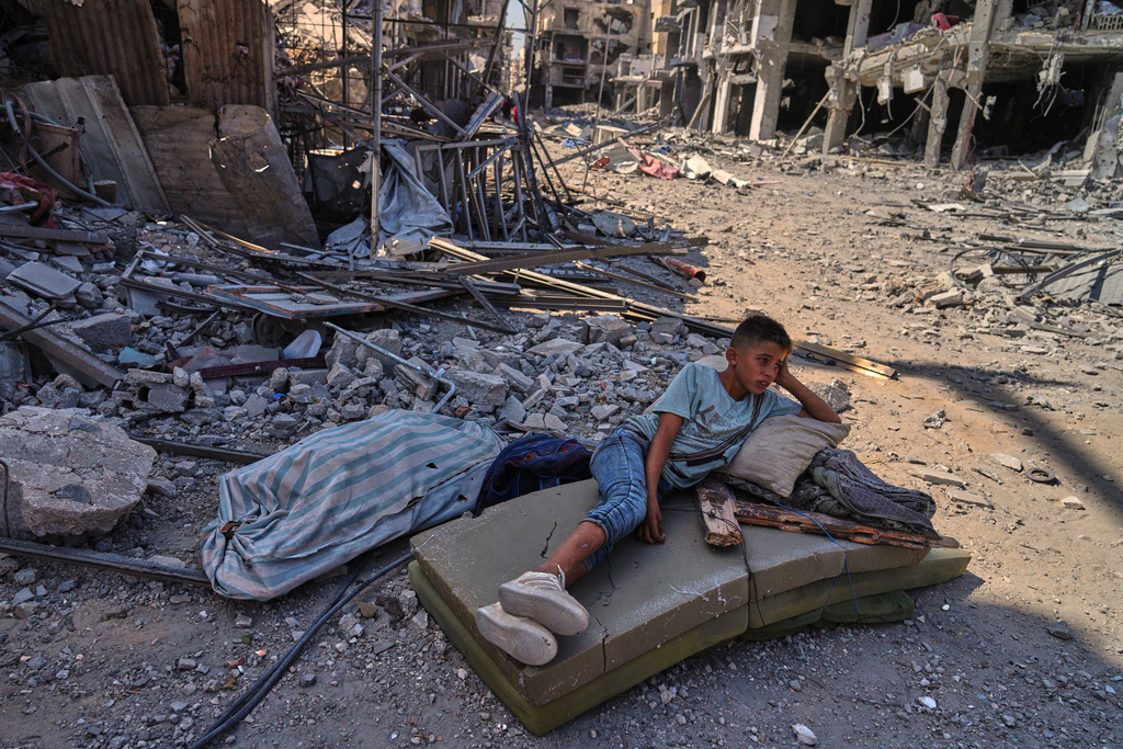 A Palestinian boy lies on a mattress amid the rubble of destroyed buildings in Khan Younis, southern Gaza Strip, Friday, Oct. 10, 2025, after Israel and Hamas agreed to a pause in their war and the release of the remaining hostages. (AP Photo/Jehad Alshrafi)