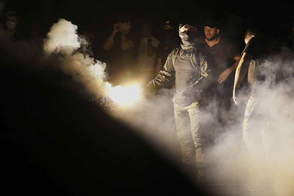 Supporters of Serbian President Aleksandar Vucic hurl flares at anti-government protesters during an anti-government protest in front of the Serbian Progressive Party office in Belgrade, Serbia, Thursday, Aug. 14, 2025. (AP Photo/Darko Vojinovic)