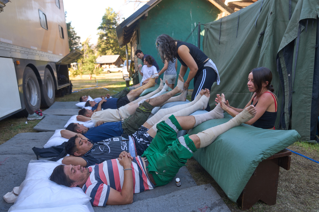 Volunteers massage firefighters resting after battling wildfires in Los Alerces National Park, Argentina, Saturday, Jan. 31, 2026. (AP Photo/Victor R. Caivano)