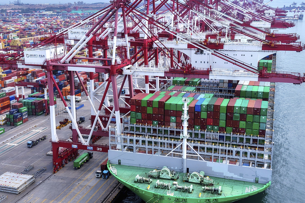 Trucks move by a vessel docked at a container terminal in Qingdao in east China's Shandong province, Monday, Aug. 11, 2025. (Chinatopix Via AP)