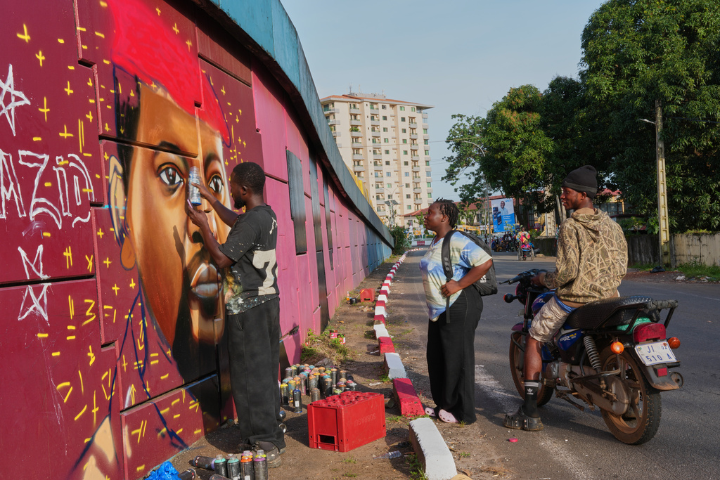 Graffiti artist Omar Diaw paints a mural of Guinea's President Mamadi Doumbouya as people stop to look in Conakry, Guinea, Saturday, Sep. 20, 2025. (AP Photo/Misper Apawu)