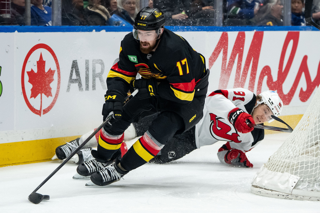 Vancouver Canucks' Filip Hronek (17) skates with the puck as New Jersey Devils' Arseny Gritsyuk (81) slides into the boards during the second period of an NHL hockey game in Vancouver, British Columbia, Friday, Jan. 23, 2026. (Ethan Cairns/The Canadian Press via AP)