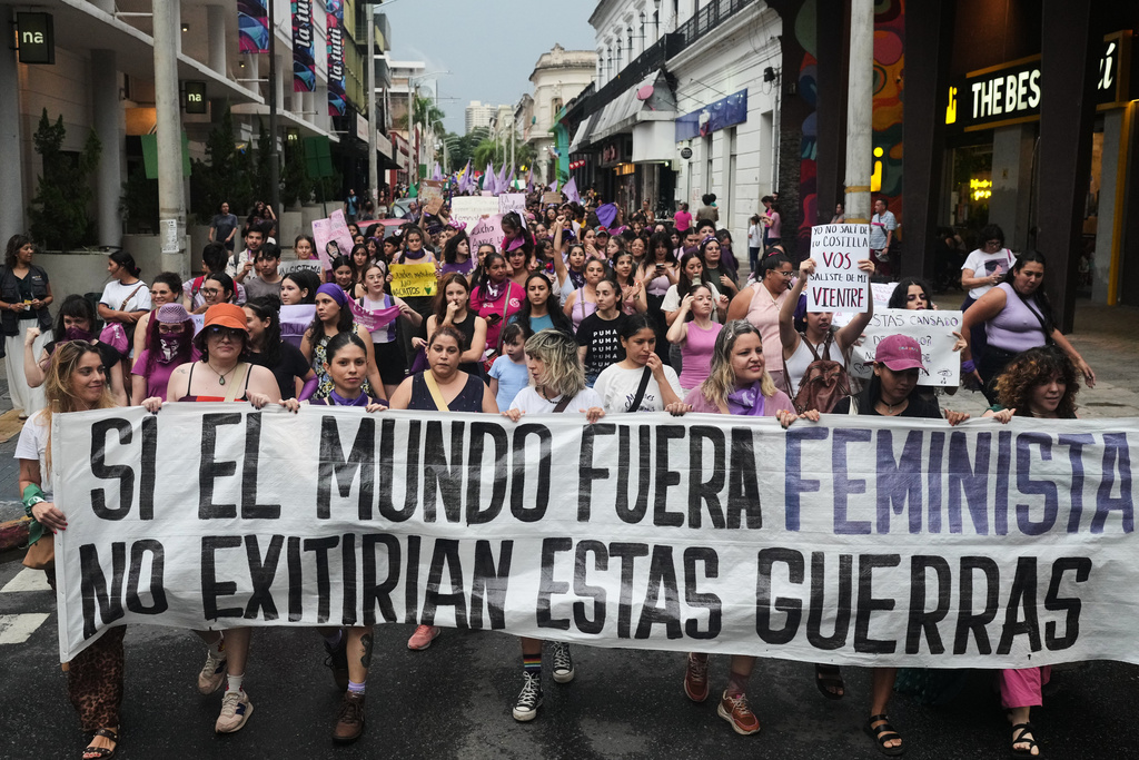 People hold a banner that reads in Spanish, "If the world were feminist, these wars would not exist" during a march marking International Women's Day in Asuncion, Paraguay, Sunday, March 8, 2026. (AP Photo/Jorge Saenz)