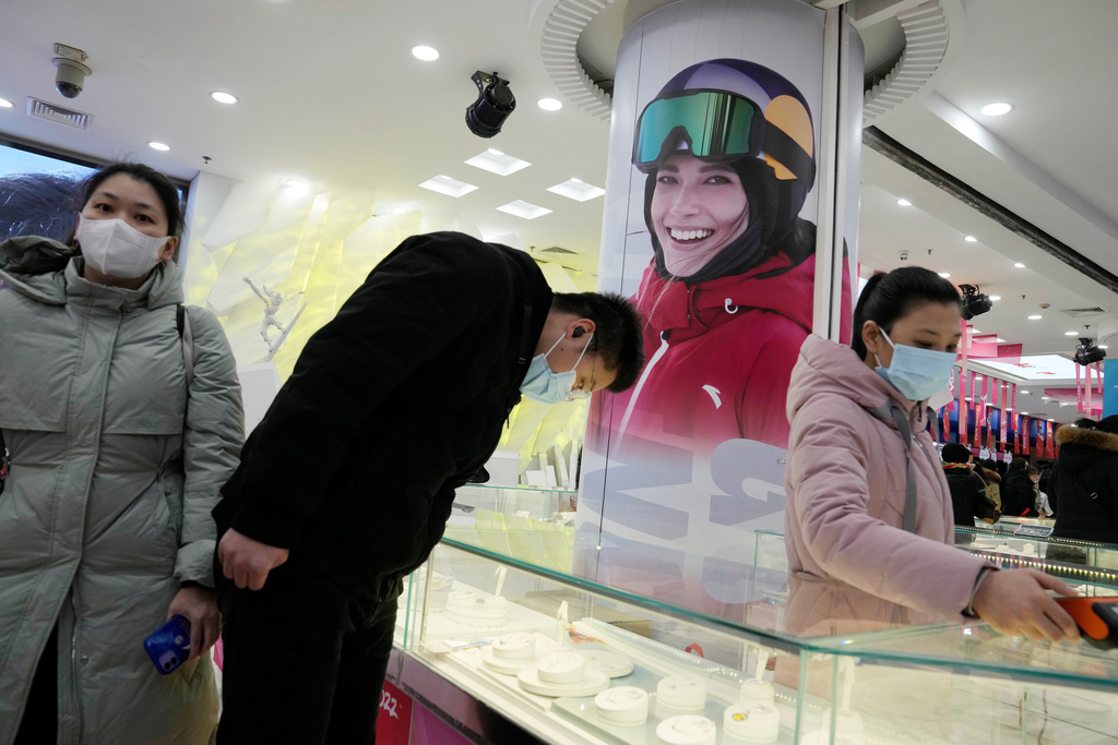 FILE - Shoppers look at official Olympics merchandise near a photo showing Chinese gold medalist Eileen Gu as the 2022 Winter Olympics nears its end, Feb. 19, 2022, in Beijing. (AP Photo/Ng Han Guan, File)