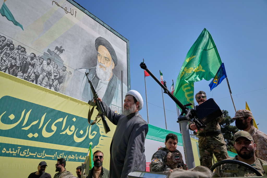 An armed Shiite cleric rides aboard a military vehicle past a billboard depicting Ayatollah Ruhollah Khomeini, founder of the Islamic Republic, during the state-organized "Janfada," or "Sacrifice for Iran," military-style parade in Tehran, Iran, Friday, Sept. 18, 2026. (AP Photo/Vahid Salemi)