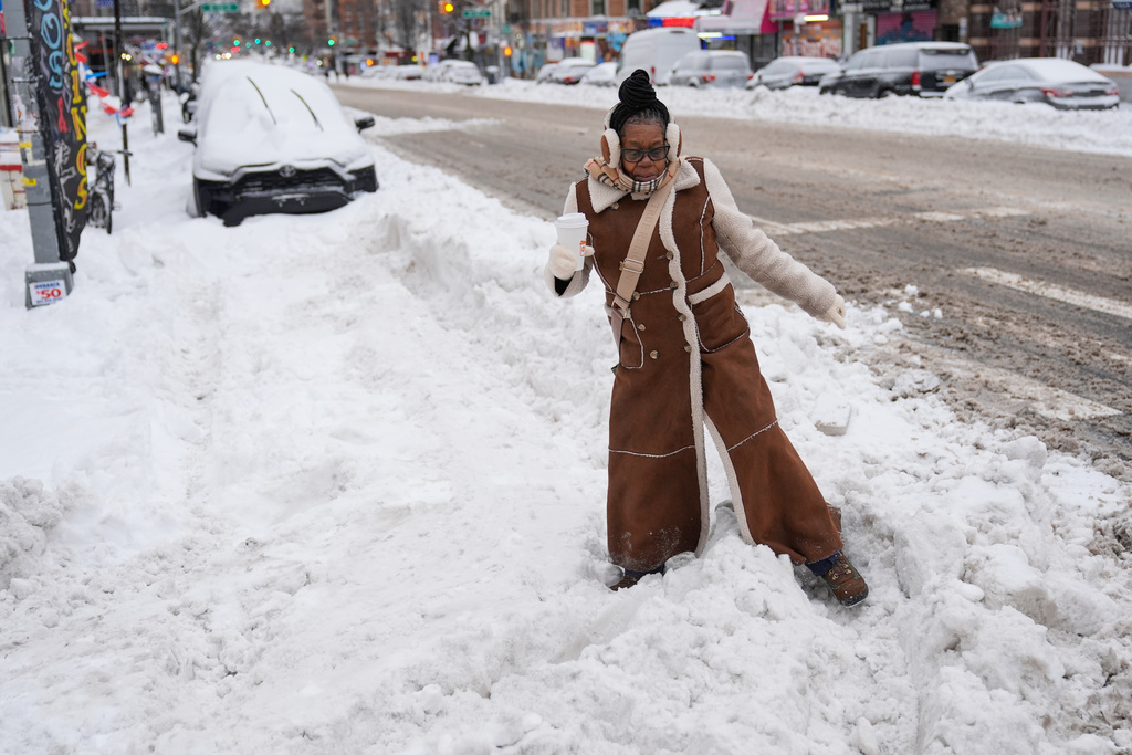 Carrie Hampton tries to navigate a snowy intersection without spilling her coffee in New York, Monday, Jan. 26, 2026. (AP Photo/Seth Wenig)