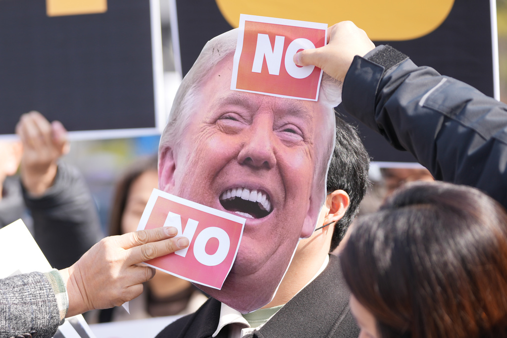 Protesters attach stickers on an image of U.S. President Donald Trump to protest against Trump's demands to multiple countries to send warships to keep the Strait of Hormuz open, near the U.S. Embassy in Seoul, South Korea, Monday, March 16, 2026. (AP Photo/Lee Jin-man)