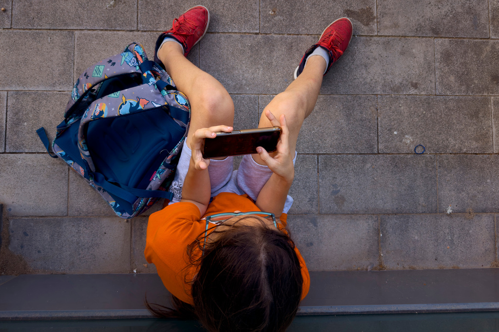 FILE - A child plays with his father's phone outside a school in Barcelona, Spain, Monday, June 17, 2024. (AP Photo/Emilio Morenatti, File)