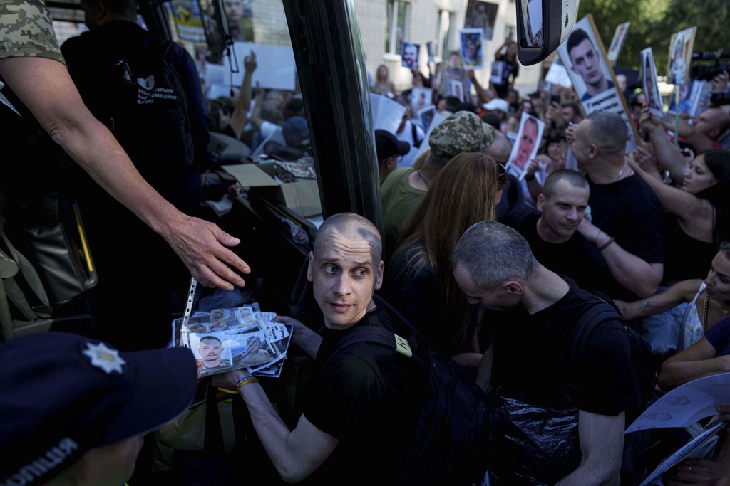 Ukrainian soldiers walk though a crowd of people holding photos of their missing relatives after returning from captivity after a POWs exchange between Russia and Ukraine, in Chernyhiv region, Ukraine, Thursday, Aug. 14, 2025. (AP Photo/Evgeniy Maloletka)