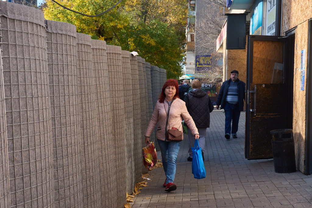Local residents keep close to the protective wall near the food market in the frontline city of Kherson, Southern Ukraine, Nov. 2, 2025. (AP Photo/Efrem Lukatsky)