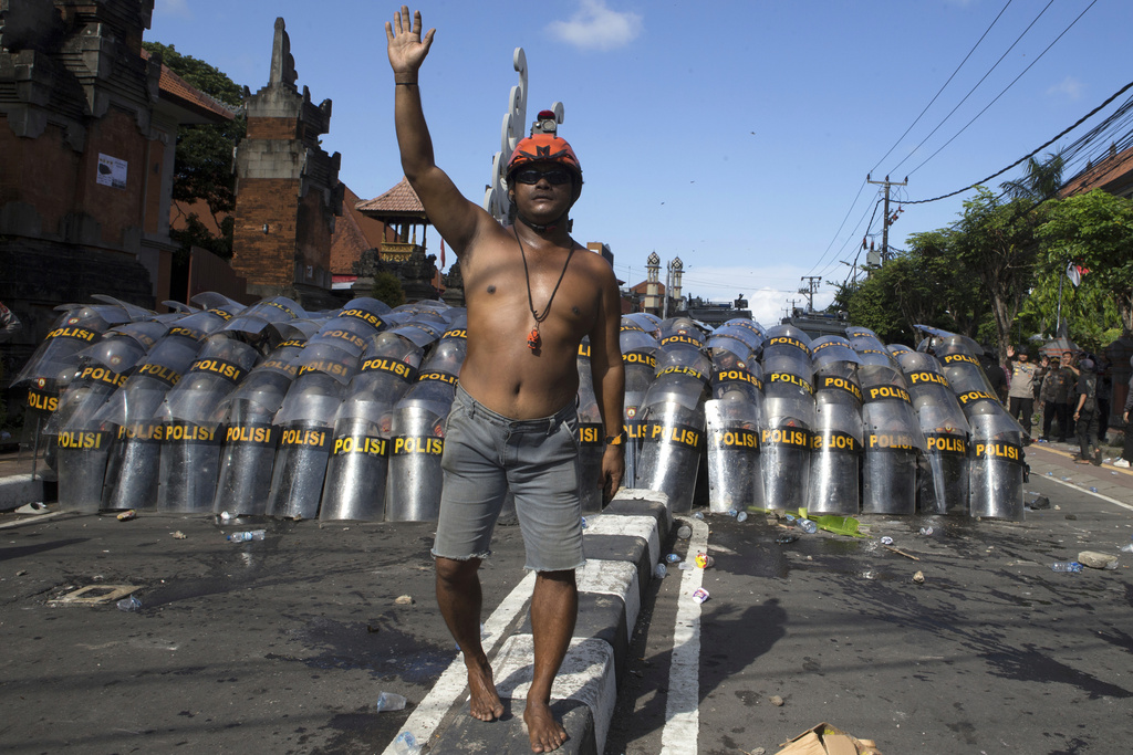A man raises his hand to calm down protesters as police officers take defensive position during a protest against lavish lawmakers' allowance, in Denpasar, Bali, Indonesia, Saturday, Aug. 30, 2025. (AP Photo/Firdia Lisnawati)