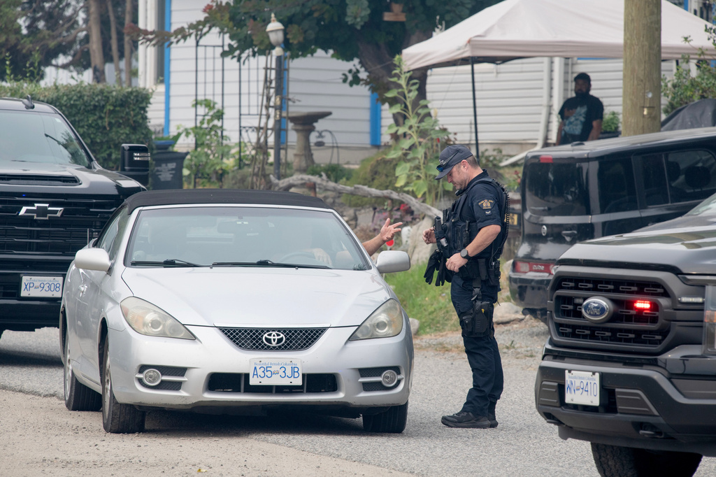 An RCMP officer talks to the driver of a car in an evacuated area on Renfrew Rd. south of Peachland, British Columbia, Canada, on Saturday, Aug. 8, 2026. (Gary Nylander/The Canadian Press via AP)