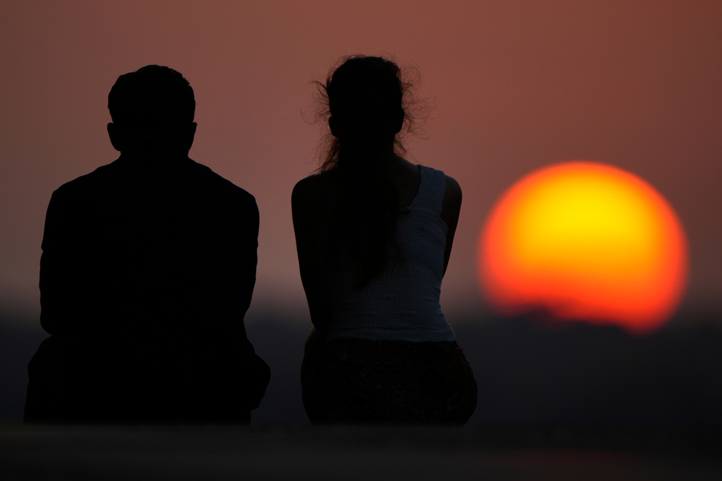 People watch the setting sun at the end of a hot summer day, Sunday, July 26, 2026, in Kansas City, Mo. (AP Photo/Charlie Riedel)