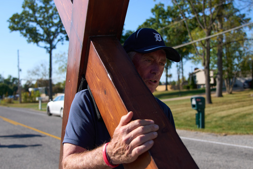 Dan Beazley, of Northville, carries a homemade cross to The Church of Jesus Christ of Latter-day Saints in Grand Blanc Township, Mich., Tuesday, Sept. 30, 2025, after a man rammed his vehicle into the building before opening fire and setting the building ablaze Sunday morning. (AP Photo/Ryan Sun) Dan Beazley, of Northville, carries a homemade cross to The Church of Jesus Christ of Latter-day Saints in Grand Blanc Township, Mich., Tuesday, Sept. 30, 2025, after a man rammed his vehicle into the building before opening fire and setting the building ablaze Sunday morning. (AP Photo/Ryan Sun)