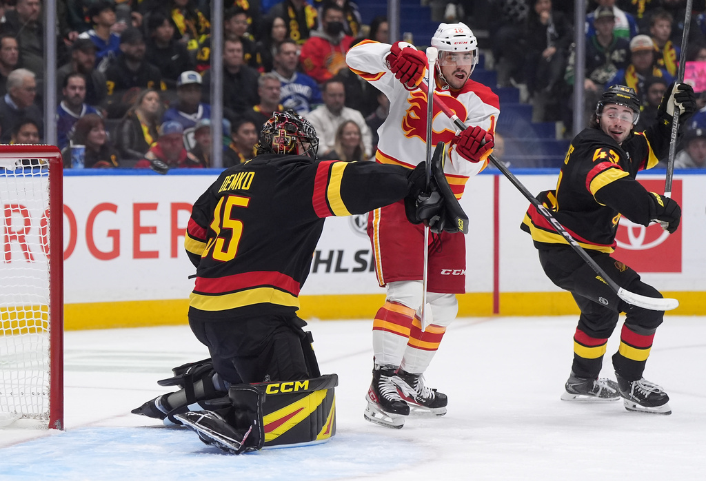 The puck deflects wide of the goal behind Vancouver Canucks goalie Thatcher Demko (35) as Calgary Flames' Morgan Frost (16) and Vancouver's Quinn Hughes (43) watch during the second period of an NHL hockey game in Vancouver, British Columbia, Thursday, Oct. 9, 2025. (Darryl Dyck/The Canadian Press via AP)