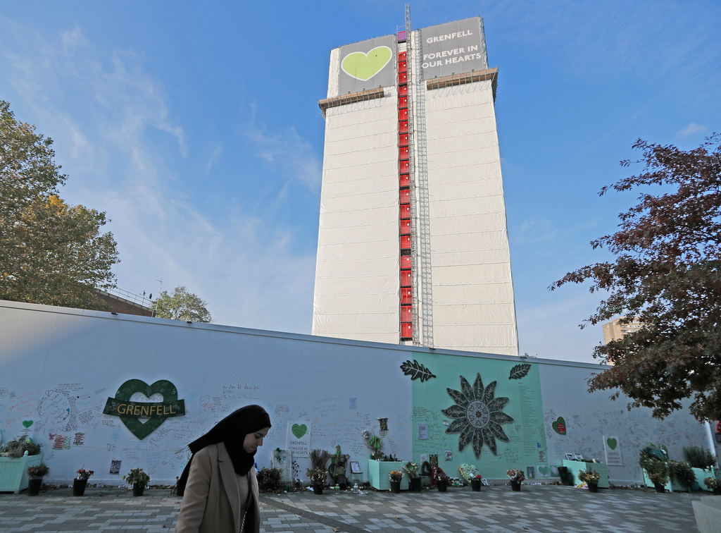 FILE - A woman passes a construction wall with written messages near Grenfell Tower in London, Wednesday, Oct. 30, 2019. (AP Photo/Frank Augstein, file)
