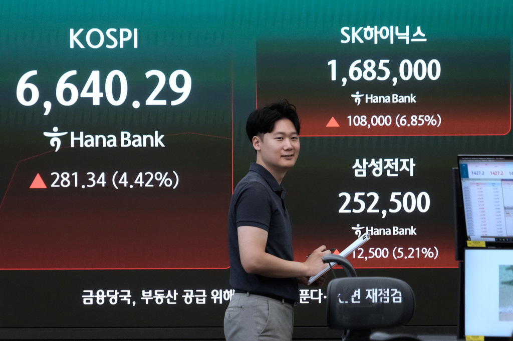A currency trader passes by a screen showing the Korea Composite Stock Price Index (KOSPI), SK Hynix and Samsung Electronics Co. stock price at the foreign exchange dealing room of the Hana Bank headquarters in Seoul, South Korea, Wednesday, Aug. 5, 2026. (AP Photo/Ahn Young-joon)
