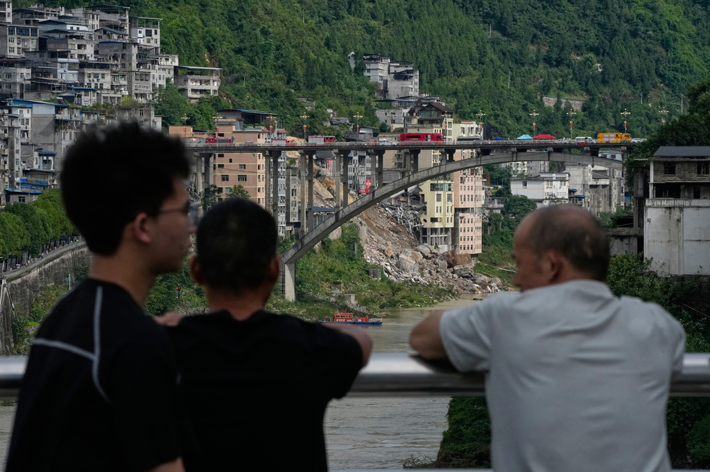Residents gather on a bridge to look at the scene of a landslide in Pengshui County in southwestern China's Chongqing on Saturday, July 18, 2026. (AP Photo/Andy Wong)