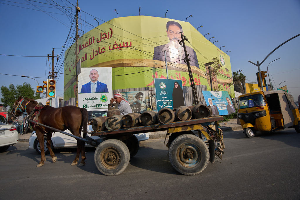 A laborer riding a horse cart carrying cooking gas cylinders, passes election posters in Baghdad, Iraq, Thursday, Nov. 6, 2025. (AP Photo/Hadi Mizban)