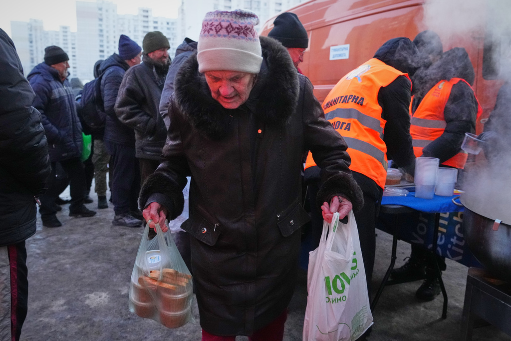 An elderly woman carries her bags out of a hot food distribution point during a power outage caused by Russia's repeated air strikes on the country's power grid, in Kyiv, Ukraine, Monday, Feb. 2, 2026. (AP Photo/Sergey Grits)