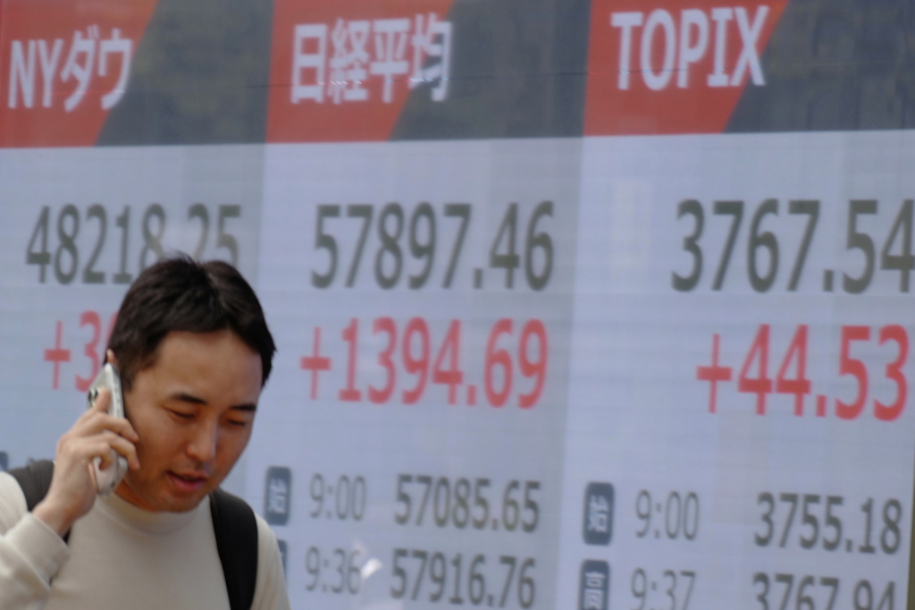 A person walks in front of an electronic stock board showing New York Dow, Japan's Nikkei, and Topix indexes at a securities firm Tuesday, April 14, 2026, in Tokyo. (AP Photo/Eugene Hoshiko)