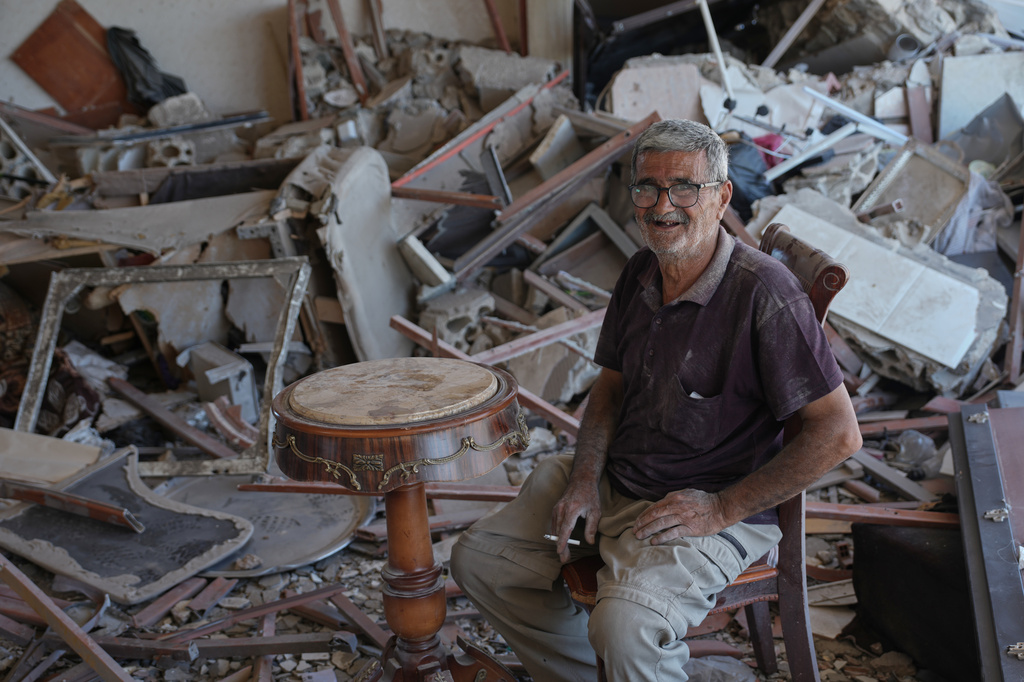 Mohammed Sobeih laughs as he smokes a cigarette while sitting amid the rubble of his home after returning to it following the Israeli military operation in Zawtar al-Gharbieh, Lebanon, Tuesday, July 28, 2026. (AP Photo/Hassan Ammar)
