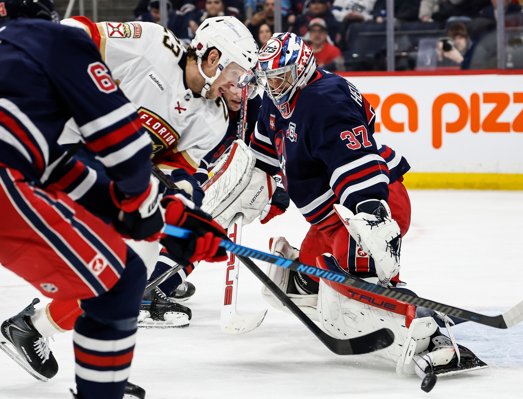 Florida Panthers' Carter Verhaeghe (23) makes a break for the net as Winnipeg Jets goaltender Connor Hellebuyck (37) and Luke Schenn (5) keep their eyes on the puck during the first period of an NHL hockey game in Winnipeg, Thursday, Jan. 22, 2026. (John Woods/The Canadian Press via AP)
