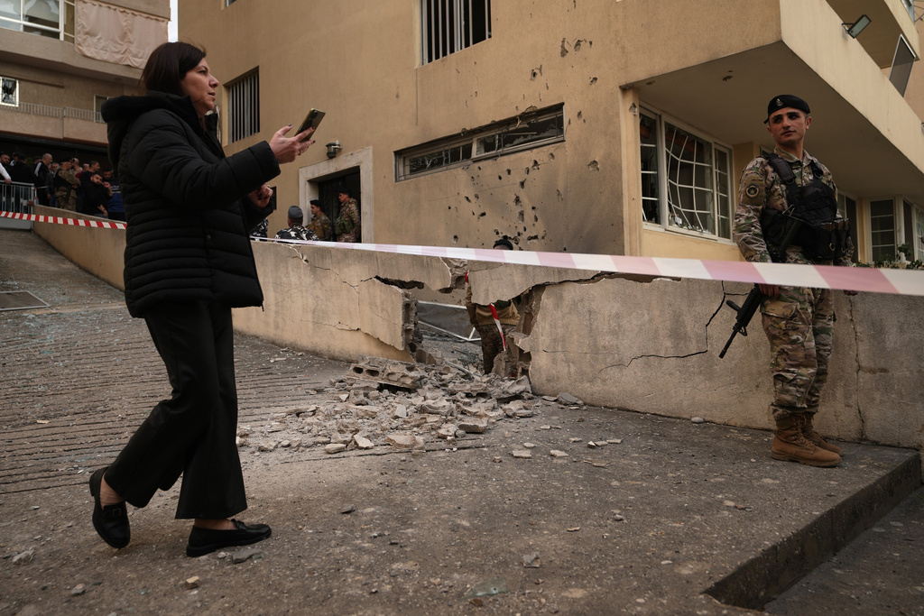 A woman passes an army soldier at the site where an intercepted missile fell in Sahel Alma, north of Beirut, Lebanon, Tuesday, March 24, 2026. (AP Photo/Hassan Ammar)